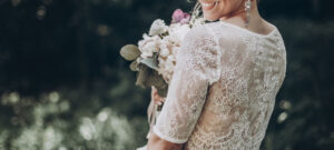 stylish wedding bride with bouquet and amazing modern dress. bride posing and smiling in sunny garden, lips and earrings close up. fine art wedding photo, romantic moment, long edge